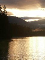 Shining sunrays reflect off the lake as surface fog lifts.